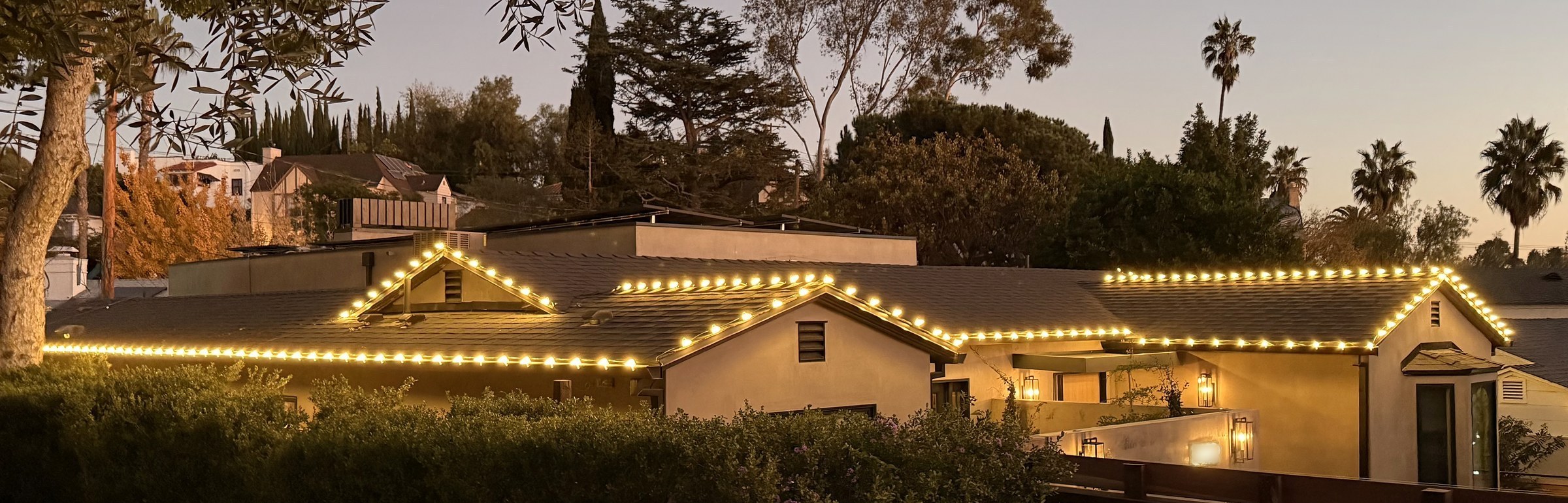 The same home at dusk, four gables outlined in lights against a violet sky and palm trees